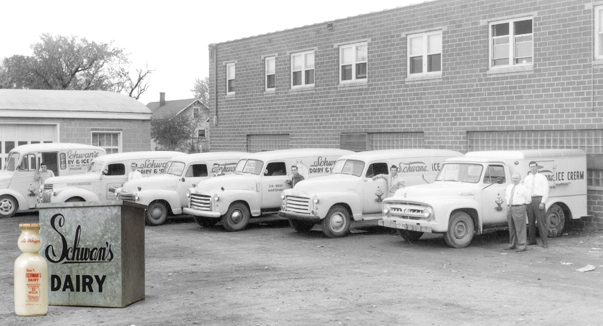 A row of six Schwan’s trucks with drivers standing next to each